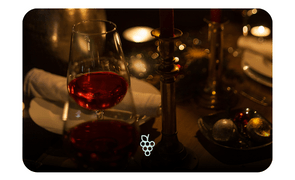 Taça de vinho tinto em mesa posta com iluminação aconchegante e decoração de velas