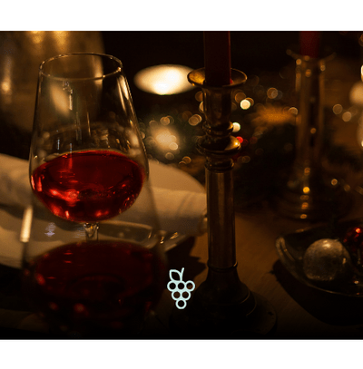 Taça de vinho tinto em mesa posta com iluminação aconchegante e decoração de velas