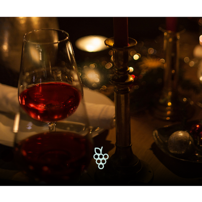 Taça de vinho tinto em mesa posta com iluminação aconchegante e decoração de velas
