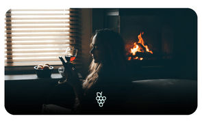 Mulher apreciando vinho tinto com lareira acesa ao fundo.